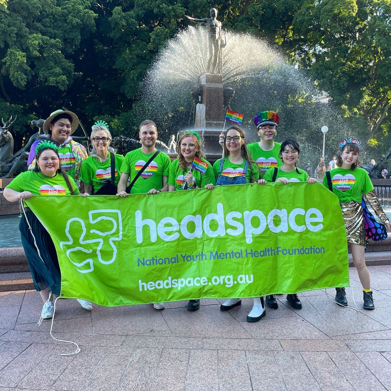 Headspace team carrying the Headspace banner at Sydney Mardi Gras — branded merchandise program supplied by Chilli Promotions including custom t-shirts, headwear and rainbow accessories